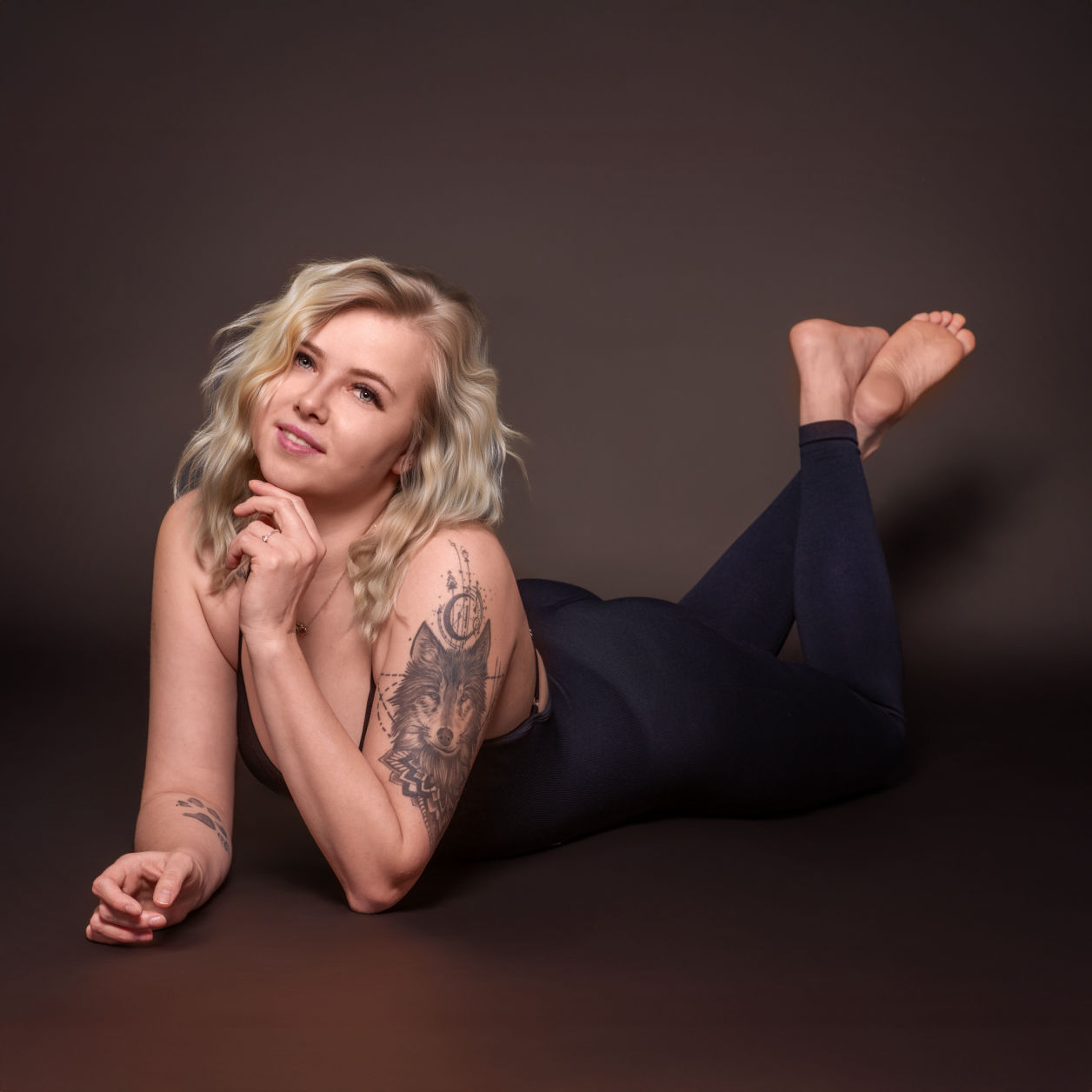 Tami beim Beautyshooting, liegt auf dem Bauch bekleidet mit einem schwarzen Bodysuit lächelt barfuss in die Kamera - Portrait Fotograf aus Geldern